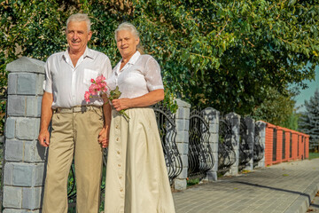 Happy active senior husband is walking with his wife. Lifestyle of couple in retirement. Elderly woman and retired man having fun together outdoors in summer