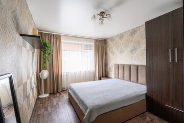 cozy bedroom with a double bed, patterned wallpaper, and wooden furniture. Natural light filters...