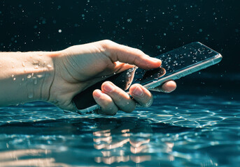 Caucasian hand holding smartphone in water with water splashing and droplets, showing phone is waterproof.