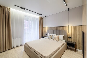 modern bedroom with a bed, bedside tables, decorative pillows, wood paneling, and a window with curtains