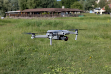 A modern drone hovers over a calm river on a sunny day. Green trees and a clear blue sky create a peaceful natural background. Concept of aerial photography, technology in nature