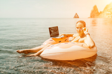 Obraz premium Woman laptop sea. Freelancer woman in sunglases floating on an inflatable big pink donut with a laptop in the sea. People summer vacation rest lifestyle concept