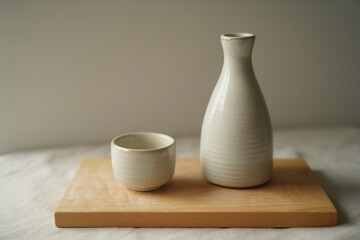 A sake set with a white bottle and a cup on a wooden board against a neutral background scene still life