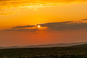Sunset Field Clouds: Sun filters through clouds over field during evening, creating golden atmosphere.