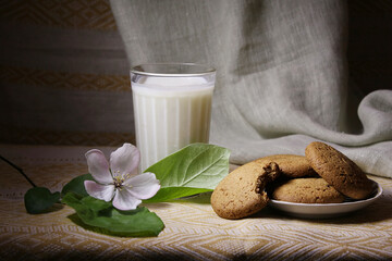 There is a glass of cream and fresh oatmeal cookies on the table
