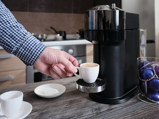 A man makes espresso coffee in a capsule coffee machine in his home kitchen.
