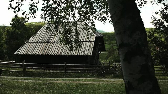 Traditional Serbian wooden barn surrounded by a wooden fence and lush greenery. Ethno village Staro Selo. Horizontal 4k footage