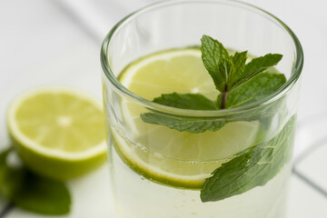 Close up of a glass of lime water with mint leaves and a lime half on a white surface