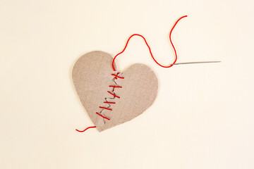 Broken cardboard heart sewed together with a needle and red thread on beige background, marriage counseling concept