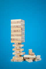 Unstable wooden blocks tower on blue background, close up with copy space