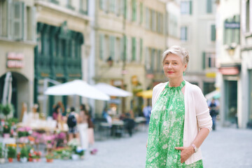 Outdoor portrait of beautiful 55 -60 year old woman posing with city background, fashion and helthy lifestyle