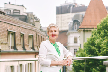 Outdoor portrait of beautiful 55 -60 year old woman posing with city background, fashion and helthy lifestyle