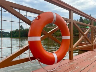 Fototapeta premium An orange and white lifebuoy hangs on a wooden bridge on a warm sunny day. High quality photo