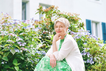 Outdoor  portrait of beautiful mature woman of 55 - 60 year old, nice short haircut with grey hair, posing with flowers background, lifestyle and fashion