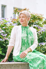 Outdoor  portrait of beautiful mature woman of 55 - 60 year old, nice short haircut with grey hair, posing with flowers background, lifestyle and fashion