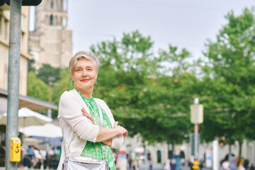 Outdoor portrait of beautiful 55 -60 year old woman posing with city background, fashion and helthy lifestyle