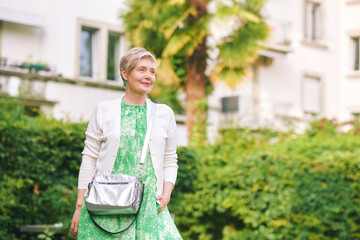 Outdoor portrait of beautiful 55 -60 year old woman posing with city background, fashion and helthy lifestyle