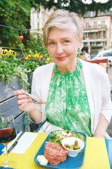 Ouutdoor portrait of elder woman eating beef  tartar  at the restaurant