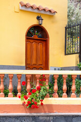 Entrance of a Canarian house with a vivid yellow facade, balustrade and rustic wooden door.