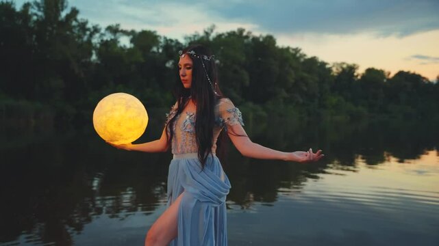 Fantasy woman holding moon magic light glowing planet in hand. Girl goddess night elf beauty face blacl long hair, river nymph wet blue dress, stands on water dark sky clouds lake. Lady fairy art. 4k