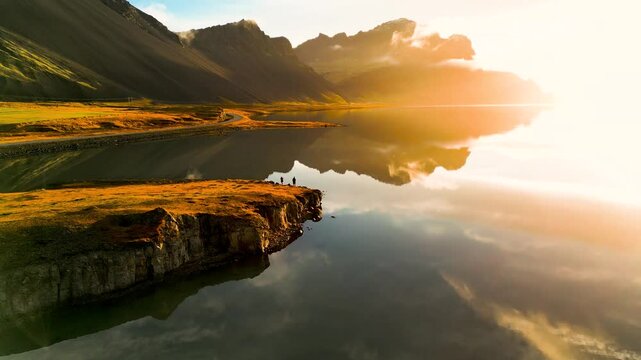 Vulkanische K&uuml;stenlandschaft in Island im goldenen Morgenlicht mit ruhiger Wasserfl&auml;che, Spiegelung der Berge und einer schmalen Stra&szlig;e entlang des Ufers in herbstlicher Umgebung