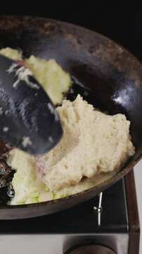 Raw potato mixture for draniki is placed onto a hot frying pan for cooking.