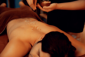 Fototapeta premium Man customer having exfoliation treatment in luxury spa salon with warmth candle light ambient. Salt scrub beauty treatment in Health spa body scrub. Quiescent