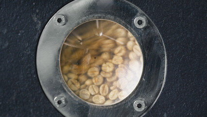 Naklejka premium Coffee beans rotating inside roasting machine at