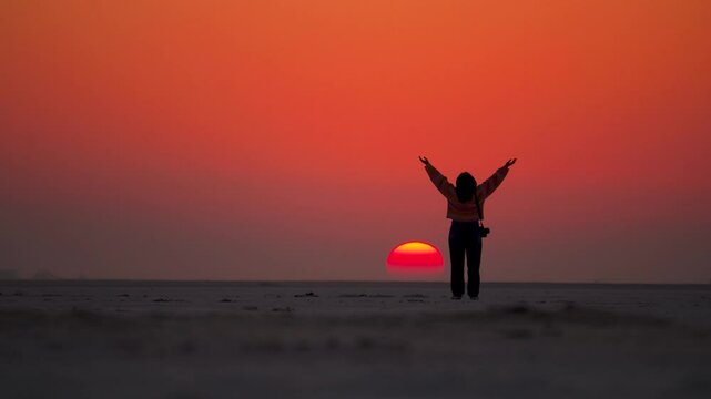 Silhouette of happy woman with raised hands over sunset sky background at White Rann of Kutch, Gujarat, India. Excited girl standing and celebrating success on a sunset background
