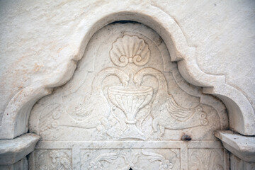 Close-up of an ornate marble relief showing two birds at a vessel, part of an old fountain in...