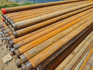 A close-up of rows of rusty drill pipes with threaded connections and protective caps, lying...