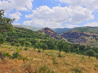 A panoramic view of green mountain ranges and foothills in Bostanliq District of Tashkent Region, Uzbekistan, stretching into the distance under a cloudy sky. 