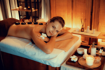 Hot stone massage at spa salon in luxury resort with warm candle light, blissful woman customer...