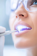 A woman is at a dental clinic receiving a tooth examination with a dental tool emitting light. Dental health and care concept