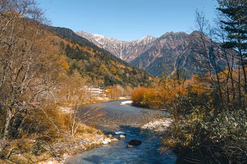 Fototapete Gebirgsfluss Landscape photo of Japan Alps with snow on top of mountain in autumn at Kamikochi, Japan. There is an emerald blue river flowing through the autumn forest. There are white and grey boulders on banks.  © Pang wrp
