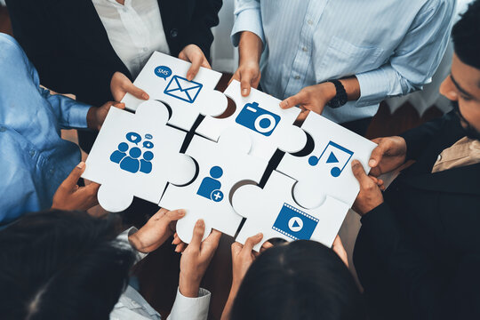 A diverse group of people collaborates by holding puzzle pieces that represent various media and communication elements, showcasing teamwork and innovation in professional environments. Amity