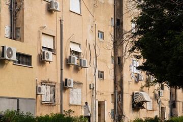 Warm-hued facade of an old apartment building with multiple air conditioners and cables, Tel Aviv, Israel