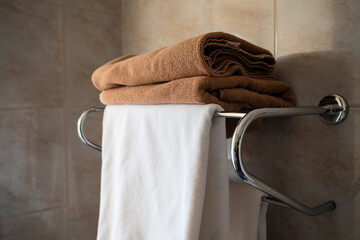 A brown and white towel are neatly folded and lying on a shelf in the bathroom