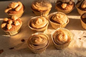 Several muffins with icing glisten in the warm sunlight. The golden lighting accentuates the layer of cream.