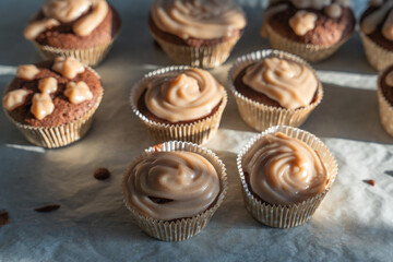 Freshly baked muffins with glossy icing cool on baking paper. The soft cream shimmers in the sunlight.