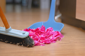 Sweeping pink rose petals with a brush into a dustpan, symbolizing the end of a romantic relationship