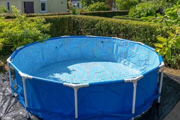 Empty above-ground pool set up in the garden, ready to be filled. Perfect summer day with lots of greenery.