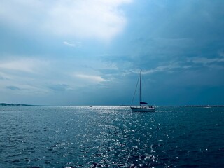 Serene seascape with a lone sailboat drifting on shimmering blue waters under a dramatic, partially...