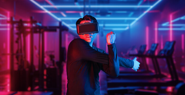 Asian man with VR glasses playing fitness while exercising at fitness. Male model using augmented reality and artificial intelligence to plan exercise plan. Technology innovation concept. Ingenuity.