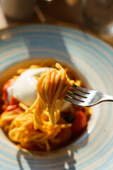 Fork lifting spaghetti with burrata and tomato sauce
