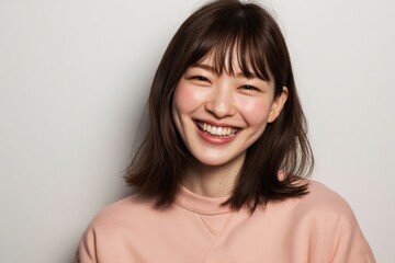 A smiling Japanese woman, wearing pastel pink cloth, expresses joy in her portrait, complemented by a white background that creates an inviting mood.