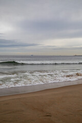 White foamy waves in a beautiful blue sea. In the distance, silhouettes of ships can be seen sailing near the coast of Gdansk on the Baltic Sea. Wave after wave rolled onto the shore. Background.