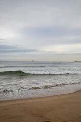 White foamy waves in a beautiful blue sea. In the distance, silhouettes of ships can be seen sailing near the coast of Gdansk on the Baltic Sea. Wave after wave rolled onto the shore. Background.