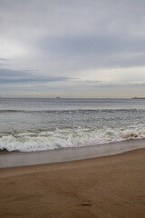 White foamy waves in a beautiful blue sea. In the distance, silhouettes of ships can be seen sailing near the coast of Gdansk on the Baltic Sea. Wave after wave rolled onto the shore. Background.