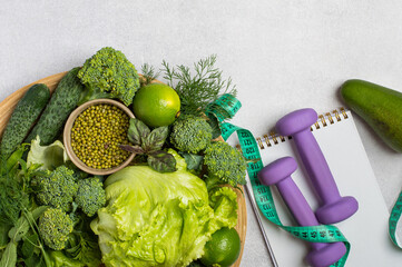 Healthy lifestyle, weight control, healthy eating, diet, lifestyle. Greenery vegetables, dumbbells and tape measure on light background.